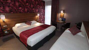 Ein Hotelzimmer mit einem großen Bett, einem kleineren Bett, einem Schreibtisch mit einem Laptop und einem Sessel.