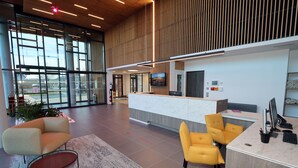 Un espace d’accueil moderne avec un comptoir en marbre, des chaises jaunes et une grande fenêtre offrant une vue sur l’extérieur.