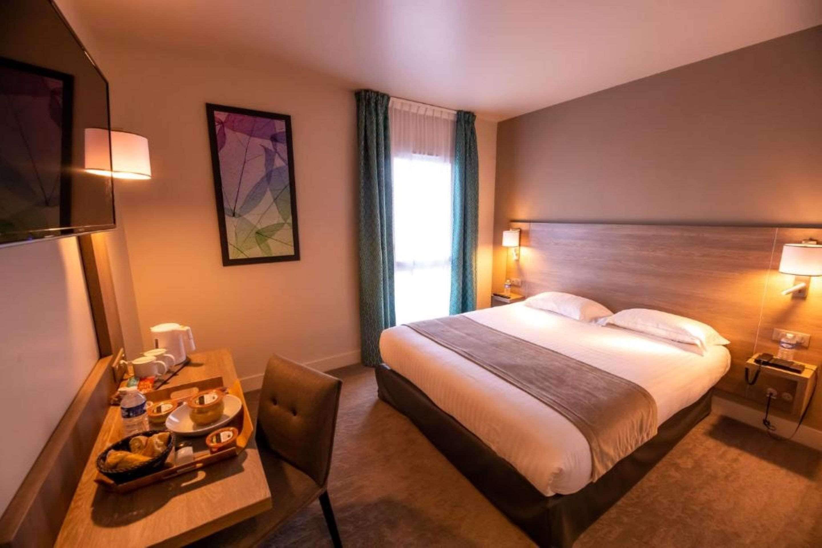 A hotel room with a bed, bedside lamps, a desk with a chair, a tray with breakfast items, and a painting on the wall.