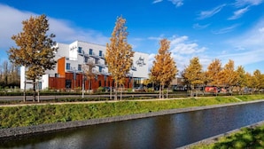Un hôtel au design moderne, situé en bord de canal, avec des arbres aux couleurs automnales.