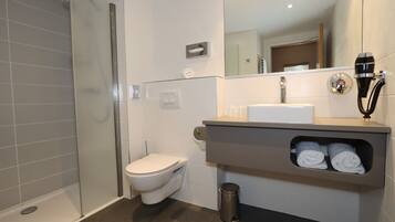 Een moderne badkamer met een douchecabine van glas, een toilet, een wastafel met handdoekhouder en een spiegel.