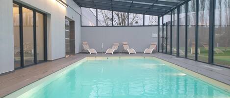 En swimmingpool med et glasomslutningsområde, liggestole og udsigt til det fri.