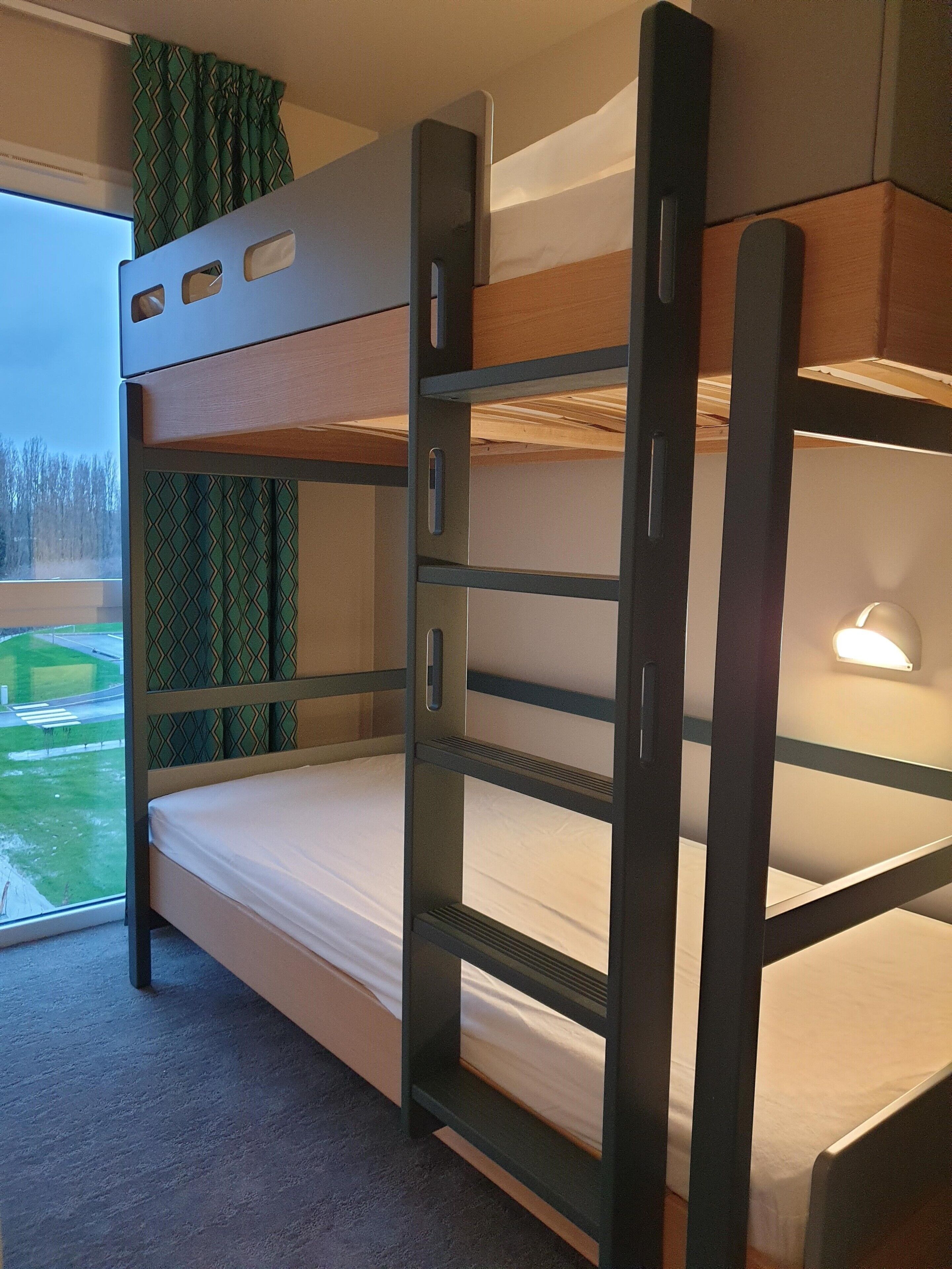 Una cama litera con vista a la ventana, una mesita de noche y una lámpara.