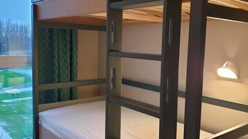 Una cama litera con vista a la ventana, una mesita de noche y una lámpara.