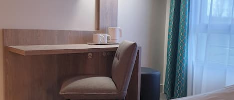A hotel room with a bed, a desk with a chair, a TV mounted on the wall, and a window with curtains.