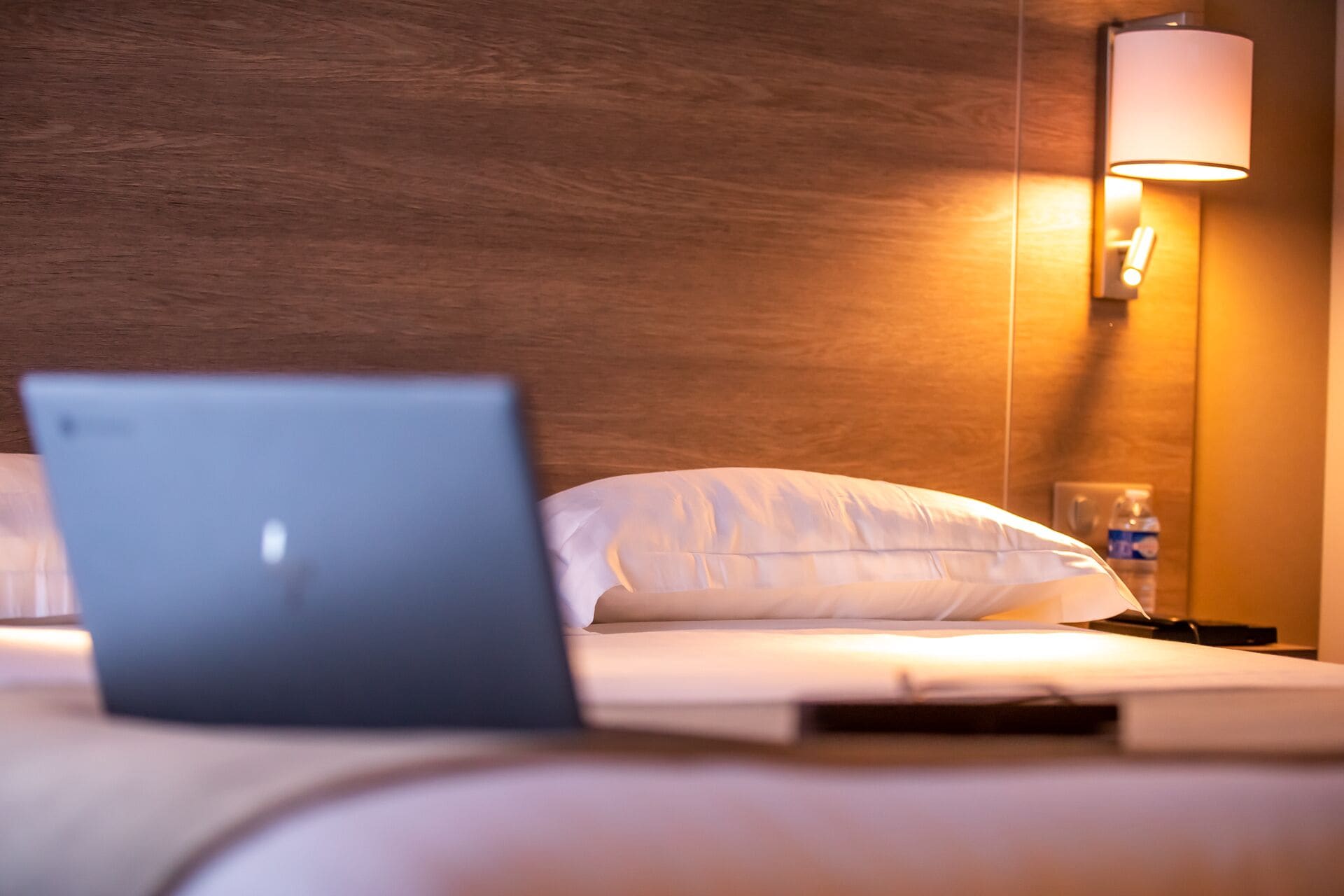 Una cama con una computadora portátil, una lámpara de noche y una botella de agua en la mesita.