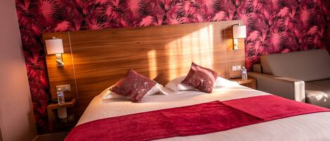 Una habitación de hotel con cabecera de madera, una cama con ropa de cama blanca y roja, dos mesitas de noche con lámparas y una manta roja.