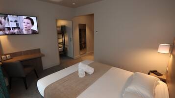 A hotel room with a bed, a desk, a chair, a TV, and a lamp.