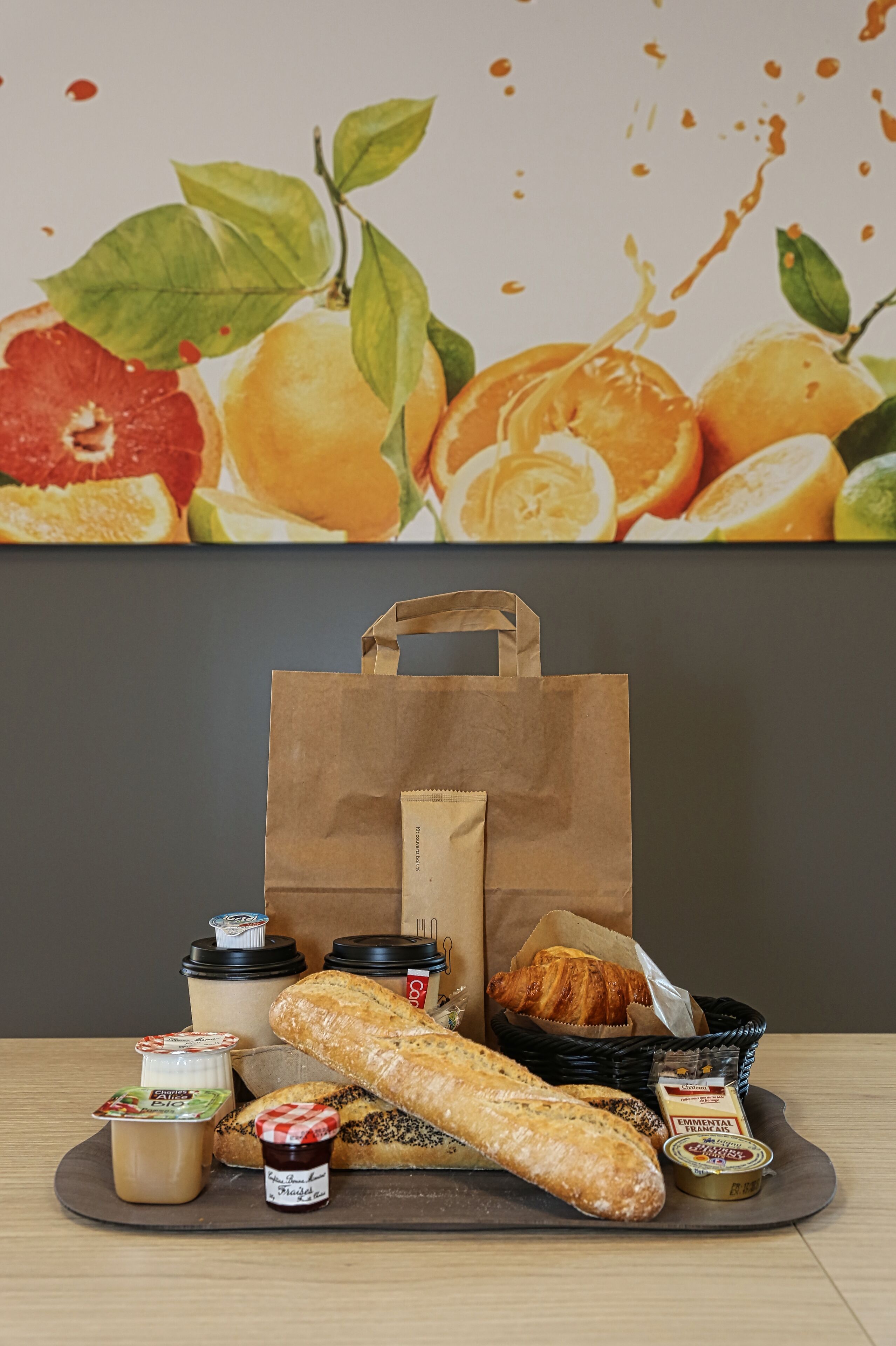 Una mesa con una baguette, un croissant y diferentes rellenos. Se ve también una bolsa de papel y una cesta.