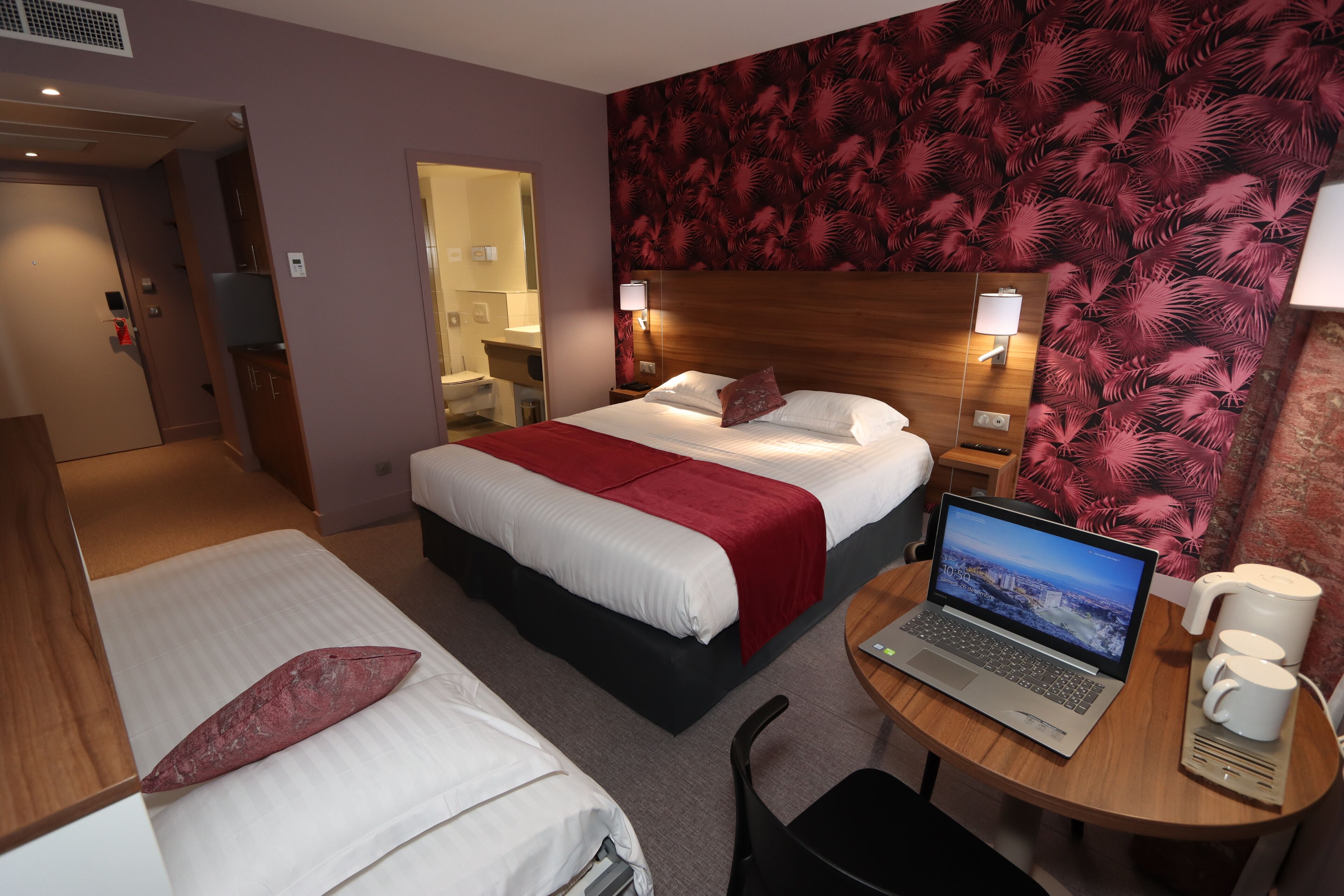 Habitación de hotel con dos camas, un escritorio con una computadora portátil y una cafetera.