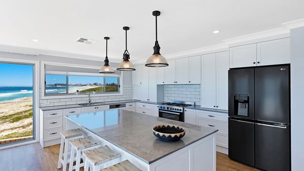 Une cuisine moderne dotée d’un grand îlot central, de meubles blancs, d’un réfrigérateur noir et de luminaires suspendus.