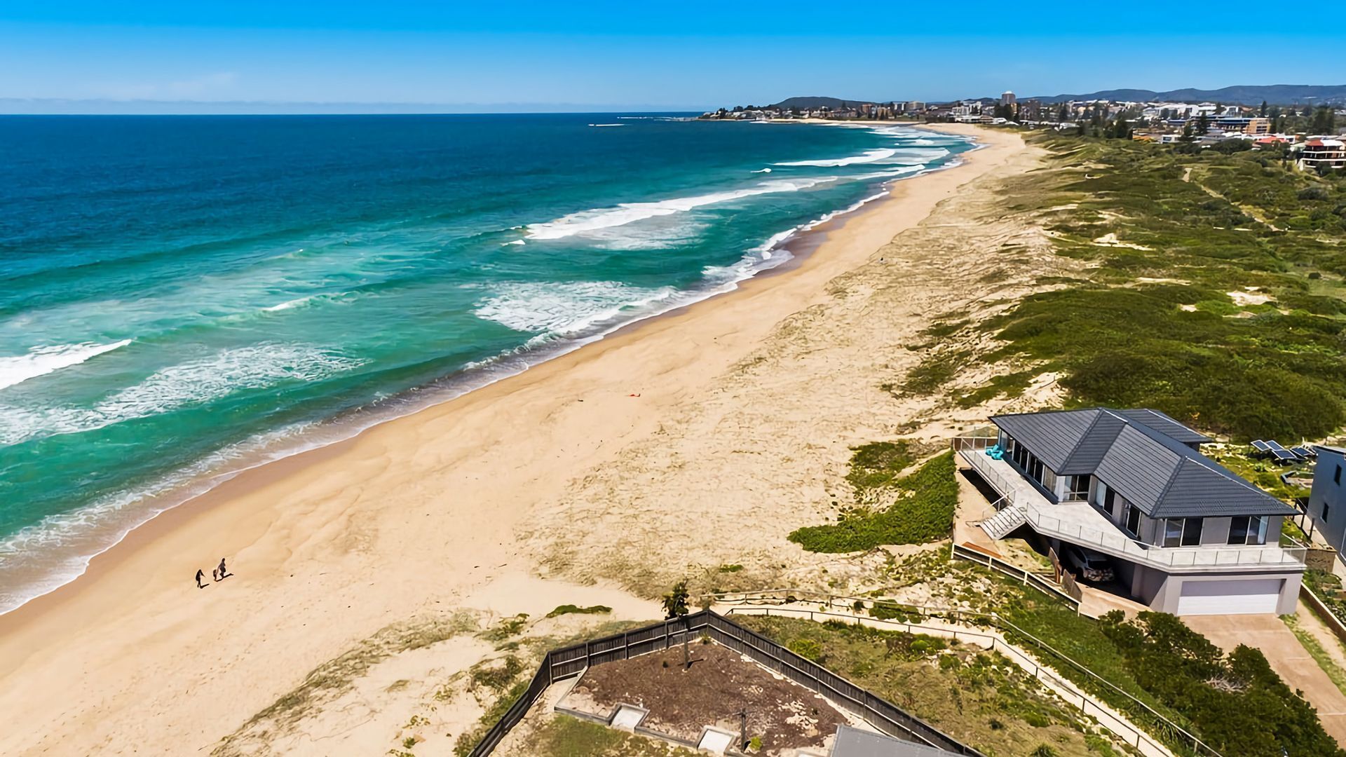 A coastal property with a beach, a modern house, and a fenced garden.