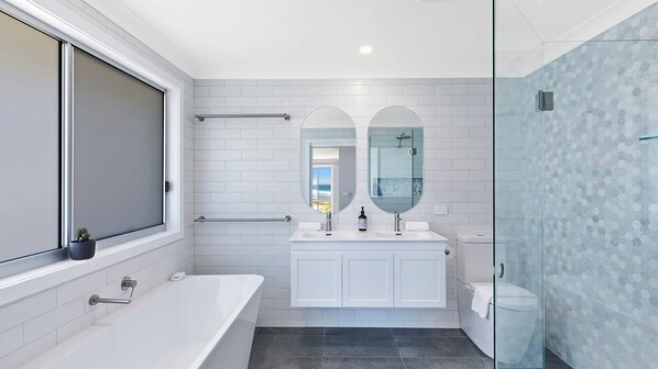 Ein modernes Badezimmer mit Badewanne, einer Duschkabine aus Glas und einem großen Fenster.