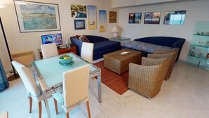 A living room with a dining table, chairs, sofas, and a coffee table. There are wall art pieces and a lamp on a side table. - Spacious 1-Bedroom Apartment with Sea View, Balcony, Pool, and Parking in Central Menton (Menton)