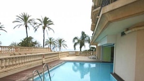 A swimming pool with a wooden deck, surrounded by a stone balustrade, palm trees, and a view of the sea. - Spacious 1-Bedroom Apartment with Sea View, Balcony, Pool, and Parking in Central Menton (Menton)