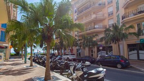 A row of parked scooters and cars on a sidewalk with palm trees and a building with balconies in the background. - Spacious 1-Bedroom Apartment with Sea View, Balcony, Pool, and Parking in Central Menton (Menton)