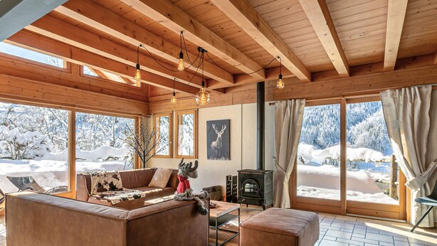 A cozy cabin interior with a fireplace, wooden beams, and large windows offering a snowy view. - Stunning Chalet for 13 - Spacious Living Area, 4 Bedrooms, Garage, WIFI - La Clusaz (La Clusaz)