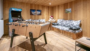A cozy room with wooden walls and ceiling, a foosball table, a sofa with a mountain pattern, and a teddy bear. - Stunning Chalet for 13 - Spacious Living Area, 4 Bedrooms, Garage, WIFI - La Clusaz (La Clusaz)