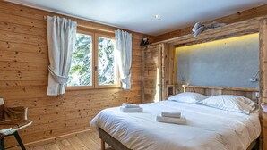 A wooden-paneled bedroom with a bed, a chair, and a window with curtains. - Stunning Chalet for 13 - Spacious Living Area, 4 Bedrooms, Garage, WIFI - La Clusaz (La Clusaz)