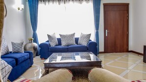 A living room with a blue sofa, a glass coffee table, and a beige armchair. - Sea La Vie (Mombasa)