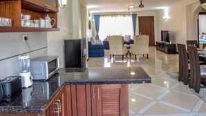 A modern kitchen with granite countertops, wooden cabinets, and a dining area with a TV and seating. - Sea La Vie (Mombasa)