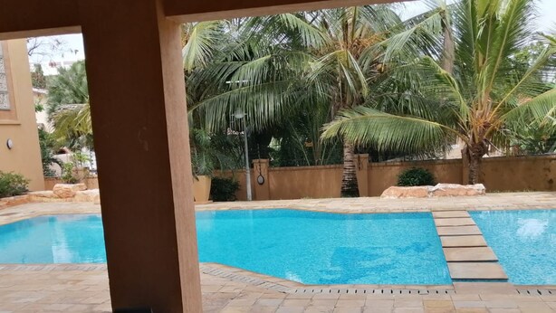 A pool area with two swimming pools, palm trees, and stone flooring. - Sea La Vie (Mombasa)