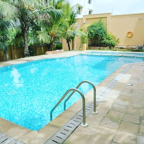 Una piscina rectangular con agua azul cristalina, rodeada por una terraza de baldosas.