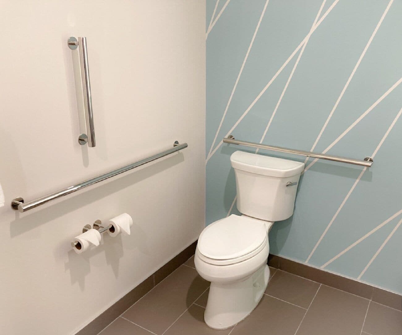 A modern bathroom with a white toilet, grab bars, and a blue patterned wall.