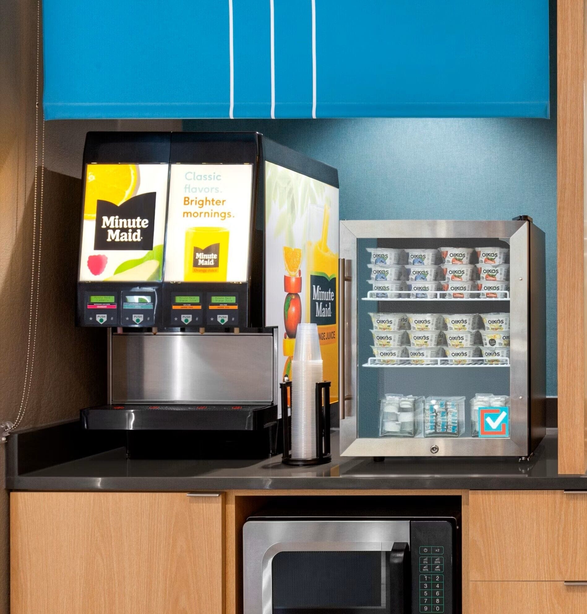 A self-service beverage station with a coffee machine and a refrigerated display of Oikos yogurt.