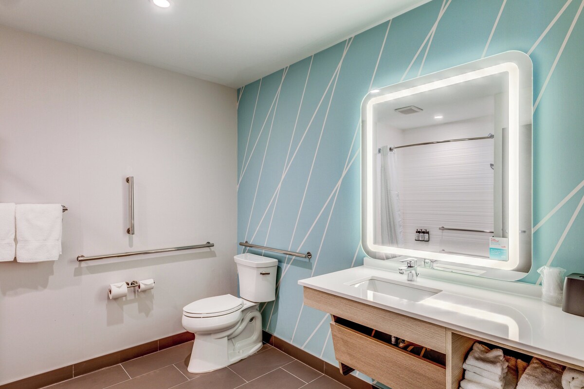 A modern bathroom with a white toilet, a glass sink, and a large mirror.