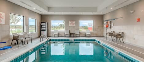 A swimming pool with clear blue water, surrounded by lounge chairs and a lifeguard on duty sign.