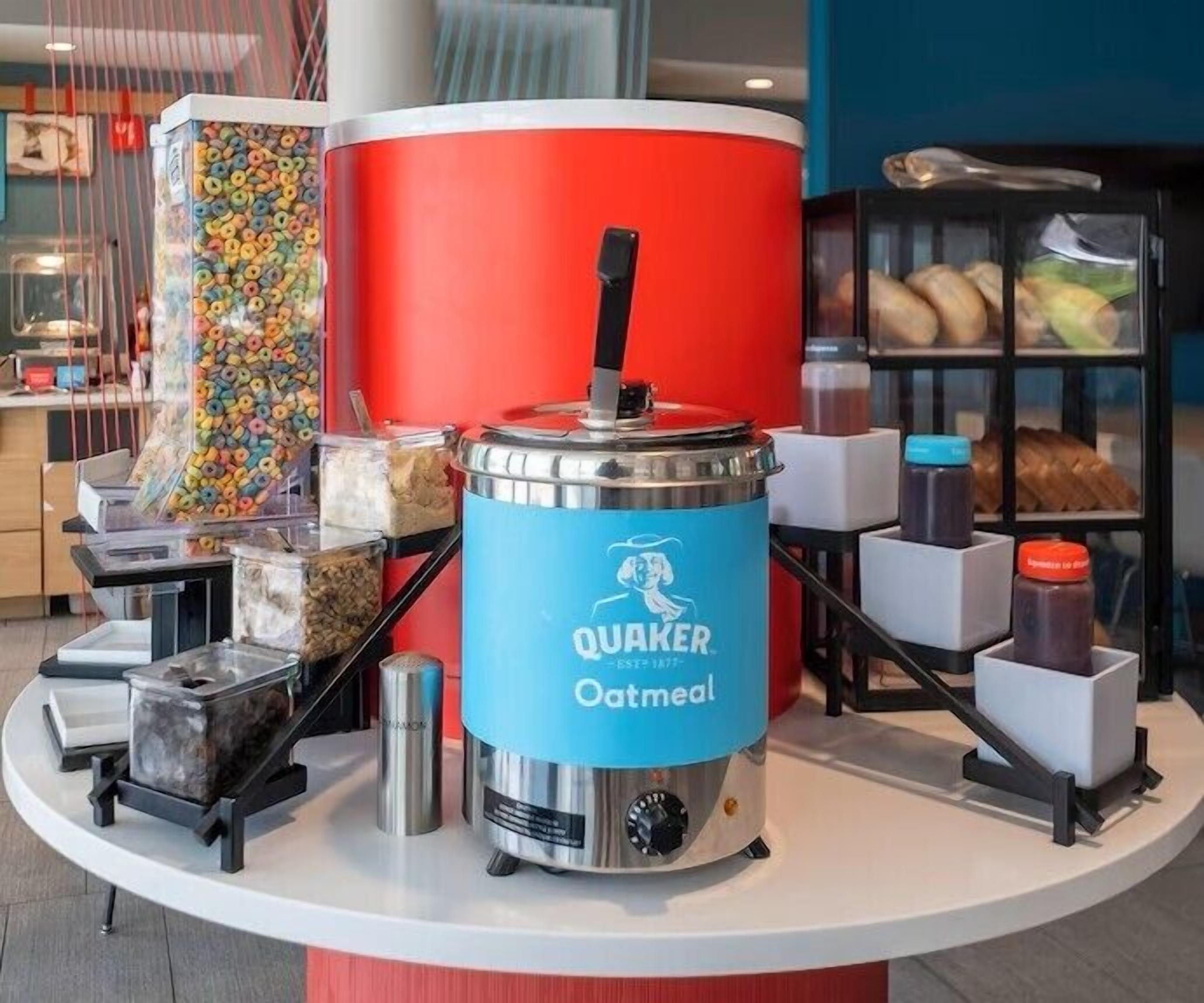 A kitchen area with a Quaker Oatmeal oatmeal dispenser, a cereal dispenser, and various food items on shelves.
