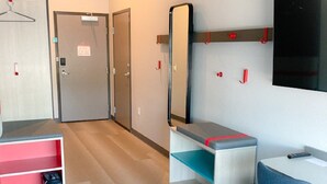 A modern hotel room with a desk, chair, and a small seating area. There is a mirror on the wall, a trash bin, and a coat rack. - avid hotel Zeeland - Holland by IHG (Zeeland)