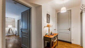 A hallway with wooden flooring, a lamp, a small table with a picture frame, and a door. - Place du Palais Historic Center (Burdeos)