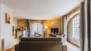 A modern living room with a sofa, TV, and stone wall. - Place du Palais Historic Center (Burdeos)