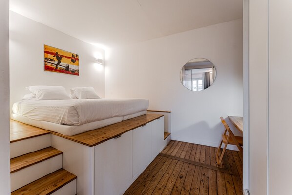 A bedroom with a bed, a wooden desk, and a round mirror on the wall.