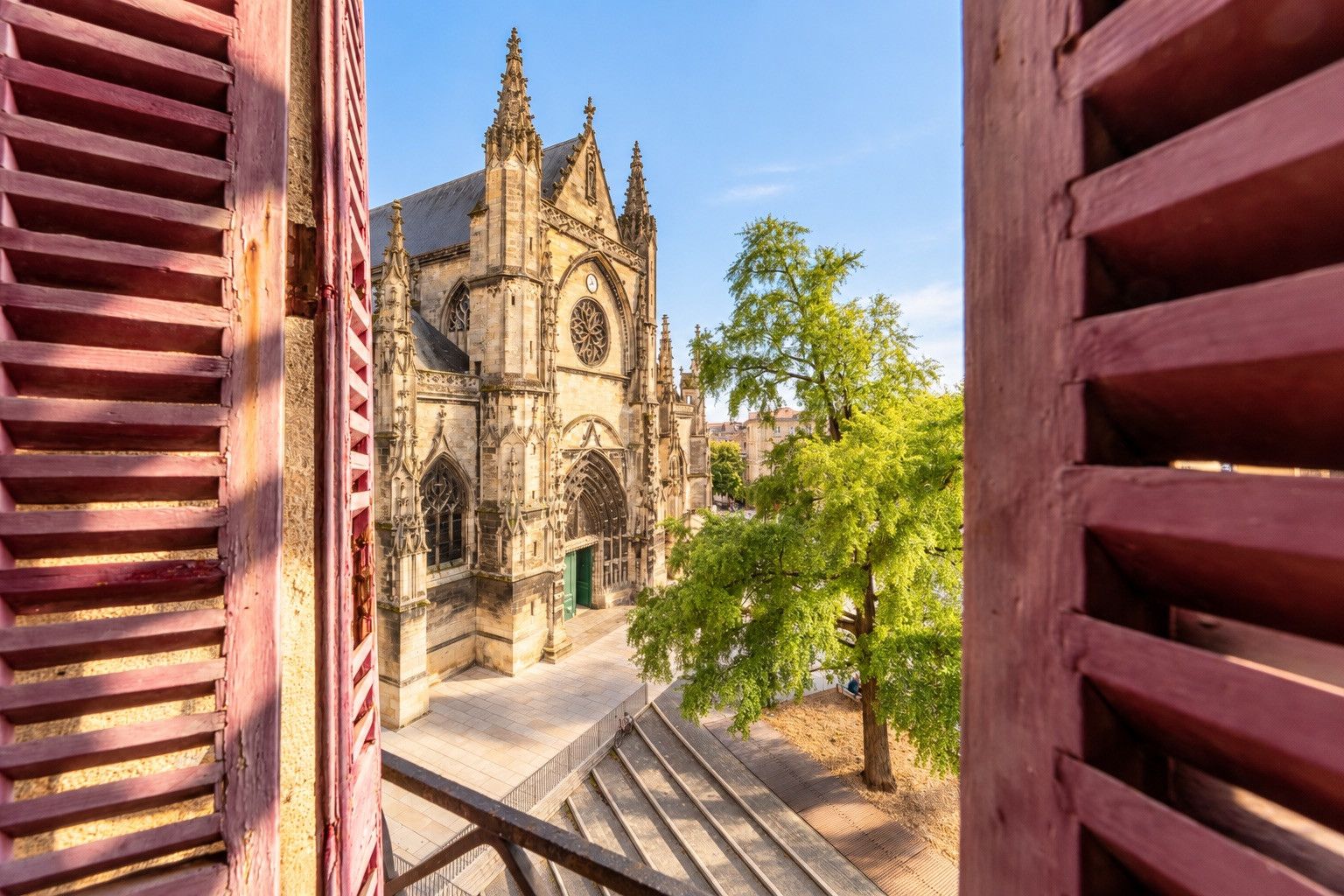 Une vue d’une cathédrale avec une porte verte, un escalier menant à l’entrée et un arbre au premier plan.