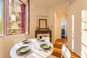 A dining area with a round table set for four, a fireplace, and a view of a historic building through a window with shutters. - Bordeaux historic center, A-C, Terrace & Parking (Burdeos)