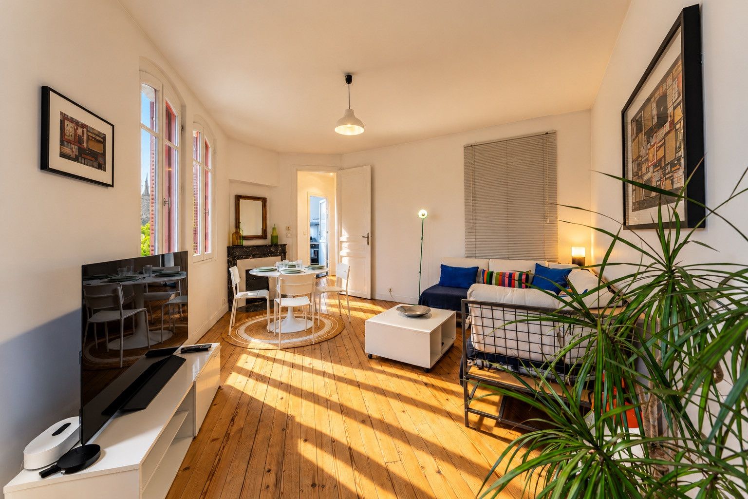 Un salon moderne comprenant un coin repas, un ensemble de canapés, un téléviseur et une grande plante.