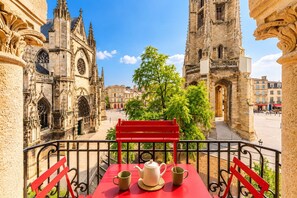 A balcony with a red table and chairs, a white teapot, and a cup, overlooking a historic building with intricate architecture.