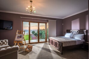 A bedroom with a large bed, a chandelier, a painting on an easel, and a view of the outdoors through a sliding door.