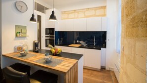 A modern kitchen with wooden countertops, a central island, pendant lighting, and a visible clock on the wall. - Luxury and comfort in the historic center of Bordeaux (Burdeos)