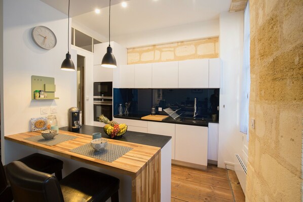 A modern kitchen with wooden countertops, a central island, pendant lighting, and a visible clock on the wall.