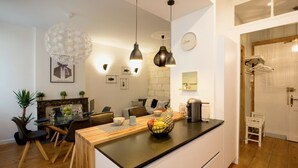 A modern kitchen with a black countertop, wooden chairs, and a dining table. There are hanging lights, a clock, and a small plant on the wall. - Luxury and comfort in the historic center of Bordeaux (Burdeos)