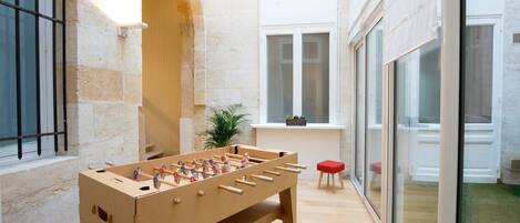A foosball table in a room with stone walls, a window, and a red stool.