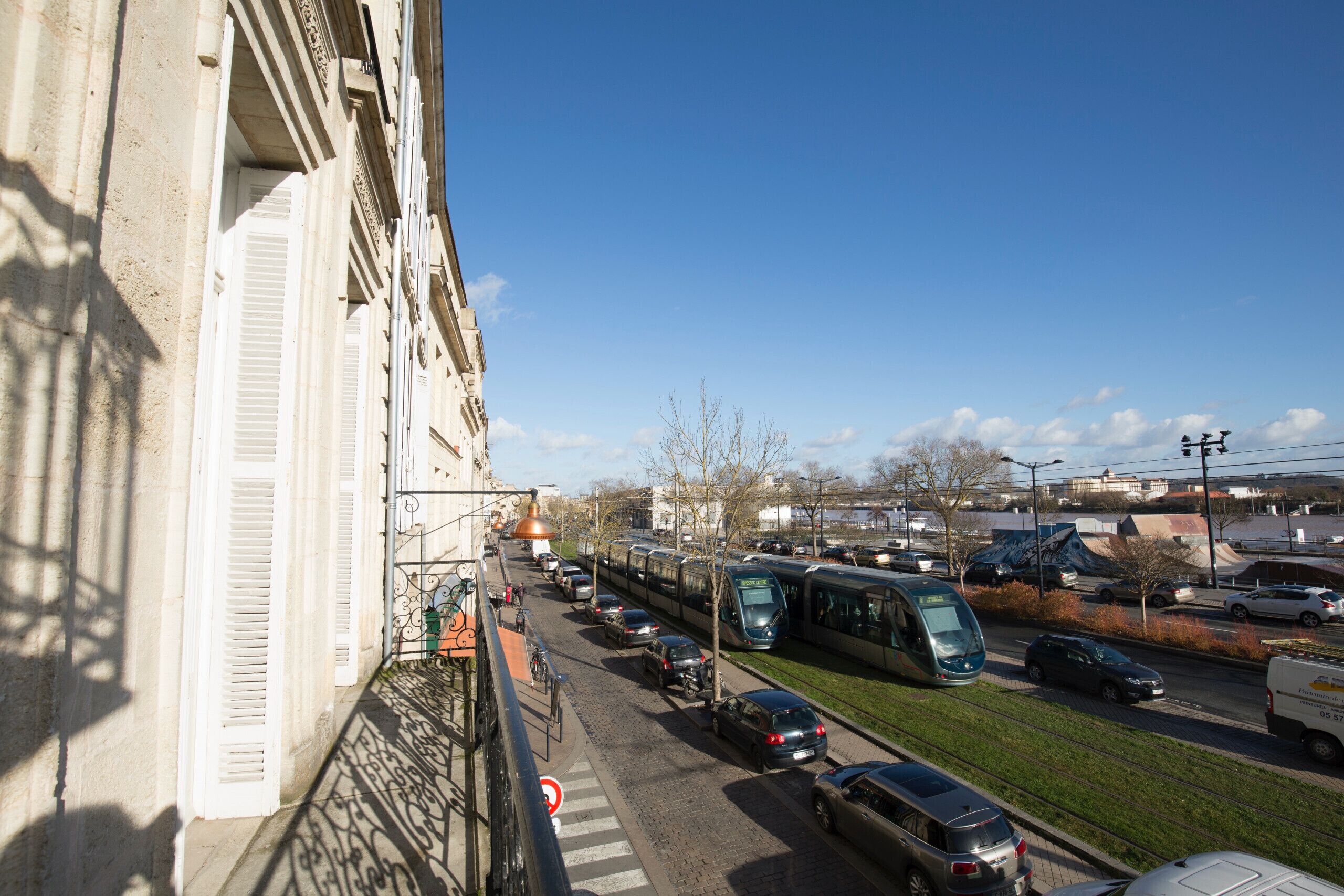 A street view with a tram, cars, and a building with white shutters.