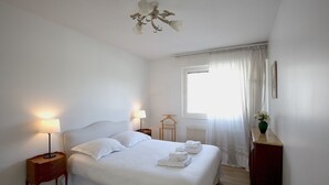 A neatly made bed with white linens, two bedside lamps, a wooden nightstand, a radiator, and a window with sheer curtains. - Spacious 2 bedrooms, Terrace, Parking, lift (Burdeos)