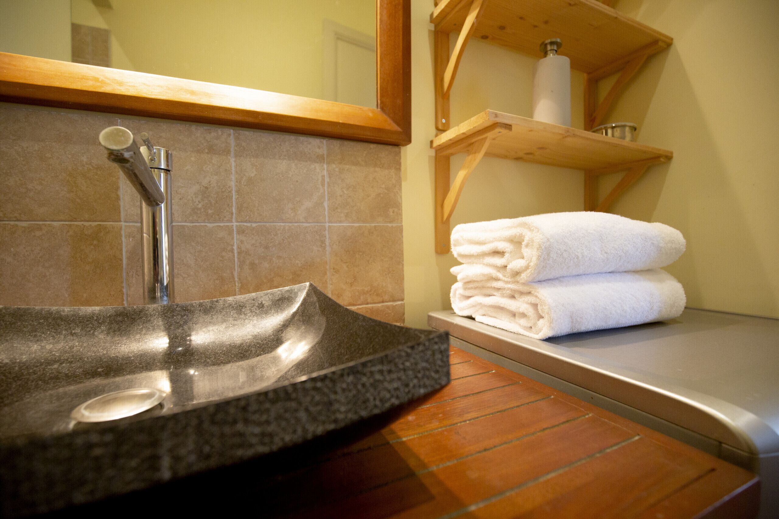Un bagno con lavabo in granito, uno specchio e uno scaffale con asciugamani piegati.