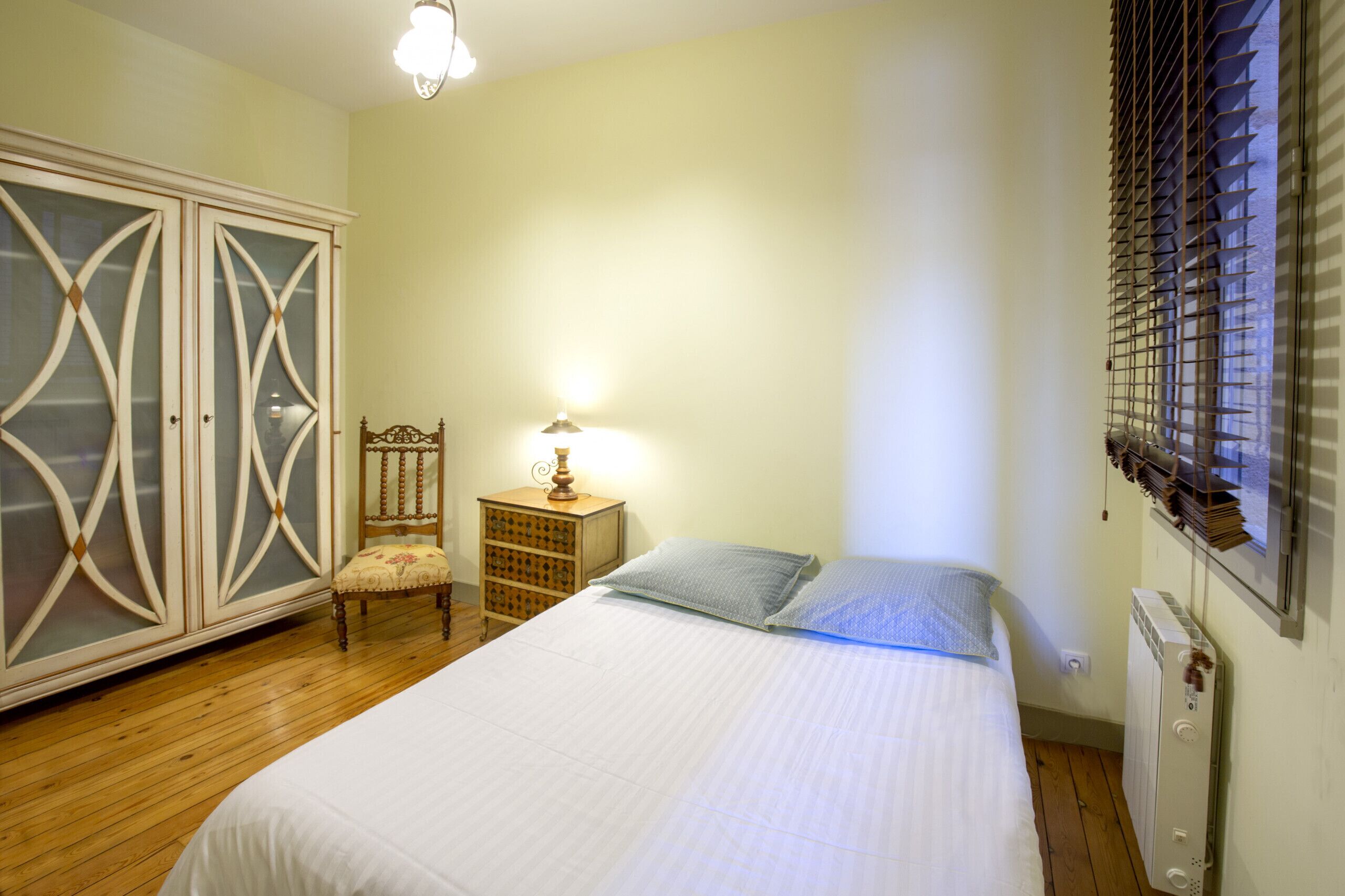 A bedroom with a bed, a chair, a nightstand, a lamp, and a wardrobe.