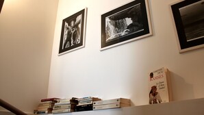 A staircase with a handrail, a wall with three framed black-and-white photographs, and a stack of books on a shelf below.